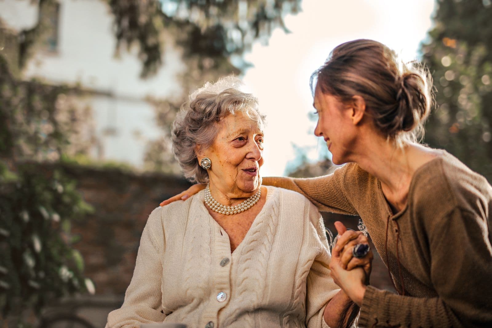 An adult daughter and her senior mother smiling together in a garden